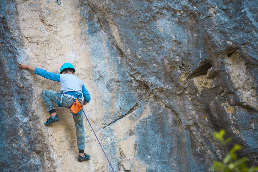 一名儿童登山者在岩石上攀爬戴头盔的男孩爬上悬崖坚强的孩子在自然浮雕上克服了艰难的攀登路线极限运动图片