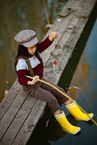 女孩坐在木制捕鱼桥上用自制捕鱼棒钓图片