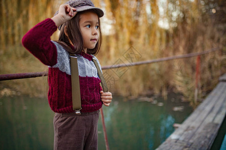 戴帽子的小女孩站在河流背景的木桥上图片