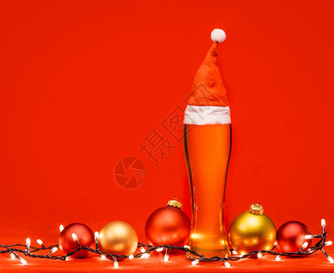 用圣诞老人或圣诞红帽圣诞灯和红色背景上的小玩意儿的全皮尔森啤酒或淡啤图片