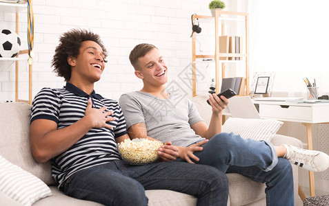 两个快乐的青少年家伙在电视上看喜剧电影在家里吃爆米背景图片