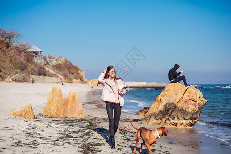 年轻女子与狗一起走路在海滨咖啡图片