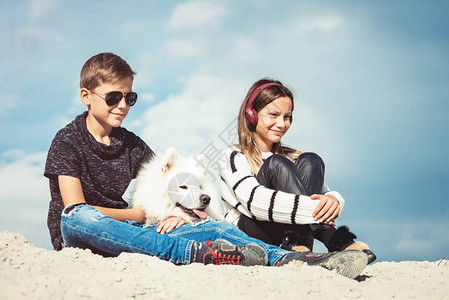 男孩和女孩在海边度假快乐的11岁男孩在海边拥抱他的狗品种萨摩耶图片