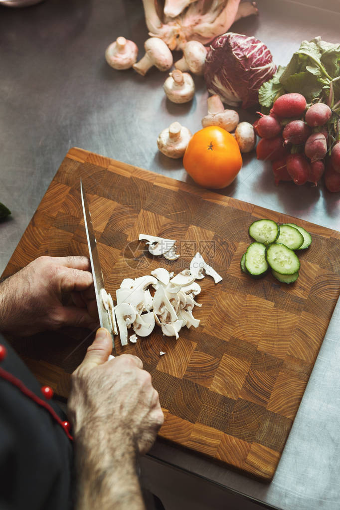 男厨师为沙拉准备蔬菜在专业旅馆或餐厅内餐室用利刃刀切蘑菇图片