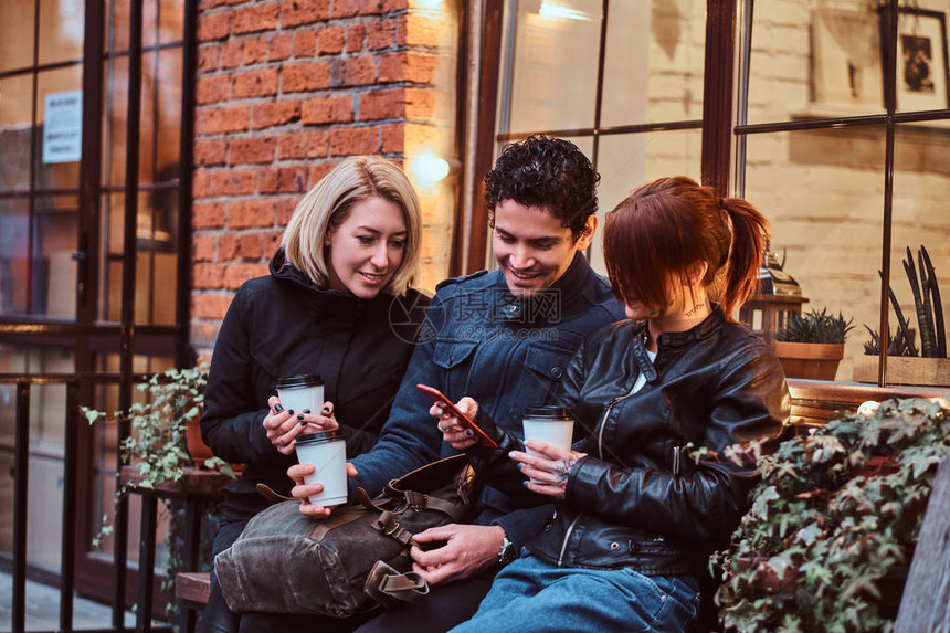 三个快乐的朋友在外边咖啡馆附近坐着时图片