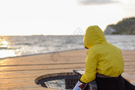 身穿黄色雨衣的女人背着黄色雨衣在日出时坐在码图片