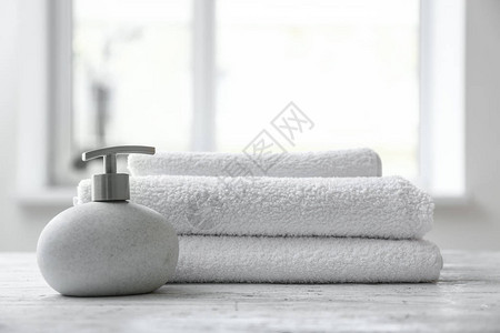 室内桌子上的液体肥皂和折叠的白色毛巾布图片