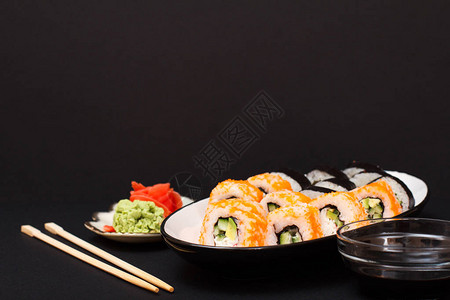 寿司卷配紫菜米饭鳄梨片黄瓜陶瓷盘上的飞鱼子板配红腌姜和芥末碗用酱图片
