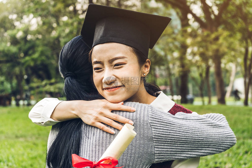 成功的学生年轻女子和单身汉礼服与文凭毕业生在大学拥抱她的朋友庆祝毕图片