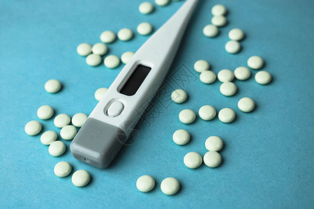 蓝色背景上的小型医用药剂圆形片剂维生素药物和电子数字温度计图片