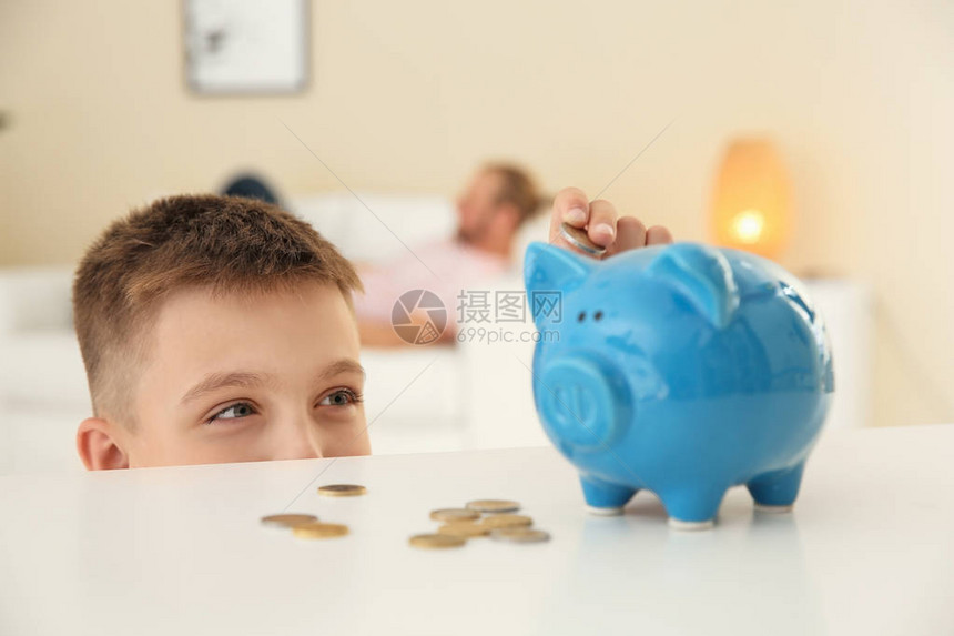 小男孩把硬币放进小猪银行图片