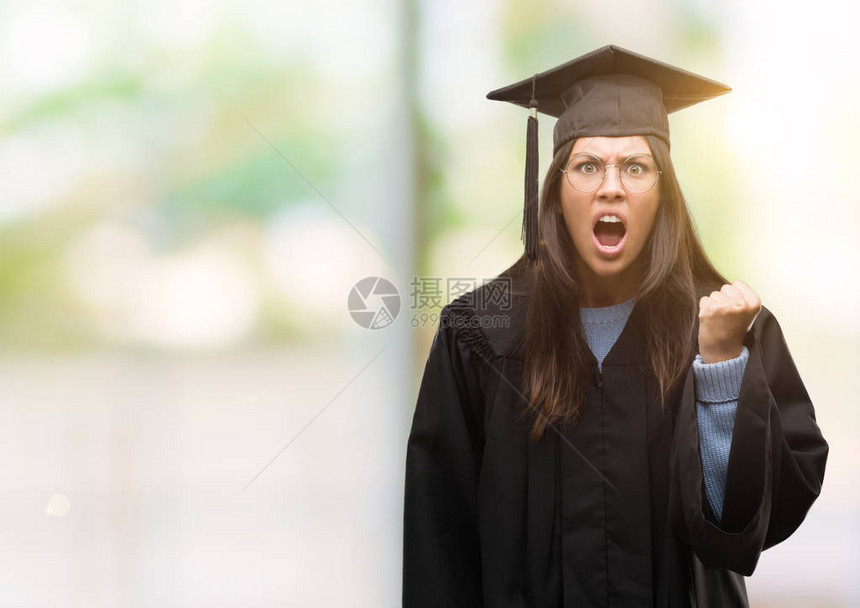 年轻的西班牙裔妇女戴着毕业帽和制服愤怒和疯狂地举起拳头沮丧和愤怒图片