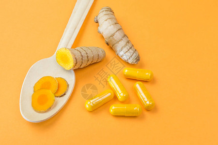 姜黄根与姜黄胶囊和橙色背景的木勺图片
