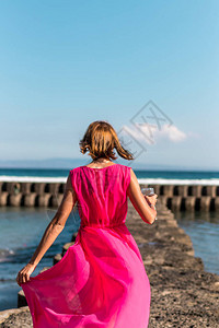 穿着长红色裙子的年轻女子和在海面背景上摆着一杯背景图片