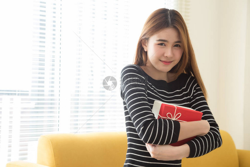 快乐美丽的亚洲女人微笑着带红色礼盒和复制空间白色客厅背景图片
