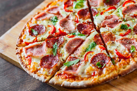 披萨配马苏里拉奶酪火腿番茄酱意大利腊肠胡椒香料和新鲜芝麻菜在木桌背景图片