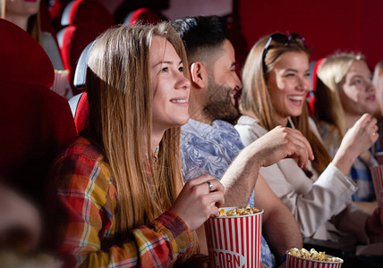 微笑美丽的女人在电影院大厅看电影害怕有吸引力的金发女郎穿着红色格子衬衫保持爆米花娱乐和电背景图片