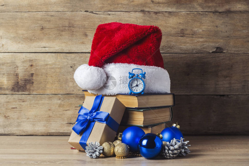 一堆书圣诞老人的帽子闹钟视锥细胞圣诞树装饰品木制背景上的礼品盒新年和圣图片