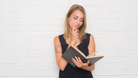 白砖墙旁的漂亮年轻美女读一本严肃的书认真地思考问题图片