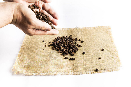 男人用手把一堆咖啡豆撒在拉菲亚布衣桌布上图片