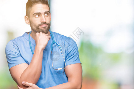 英俊的年轻医生外科医生在孤立的背景下用手托着下巴思考问题背景图片