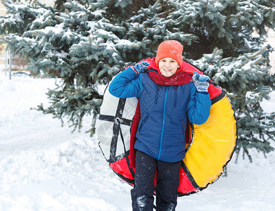 戴着帽子红围巾和蓝色夹克的开朗可爱的小男孩在雪地上拿着管子图片