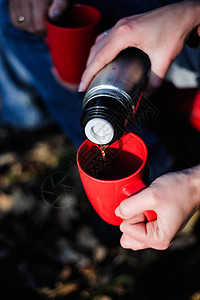 女人的手在冬季森林背景上从热水瓶中倒出热茶或咖啡女孩在雪山上使用图片