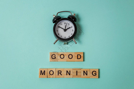 简单的平躺设计闹钟和题词早安字母在蓝色柔和的彩色时尚背景上早餐时间早上好醒概念顶背景图片