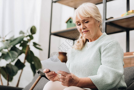 悲伤的退休妇女在客厅里拿着照片图片