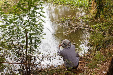 戴帽子的男人正在一个小池塘里钓鱼图片