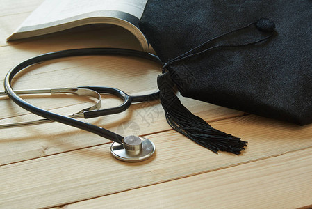 一本打开的书上的毕业帽和木制背景上的黑色听诊器从医图片