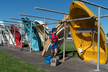 身穿红色救生衣蓝桶和渔具的小男孩在新西兰的Tauranga码头钓鱼时图片