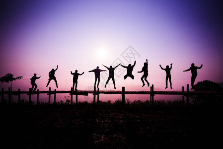 剪影跳跃队朋友在山上的木桥上跳跃图片