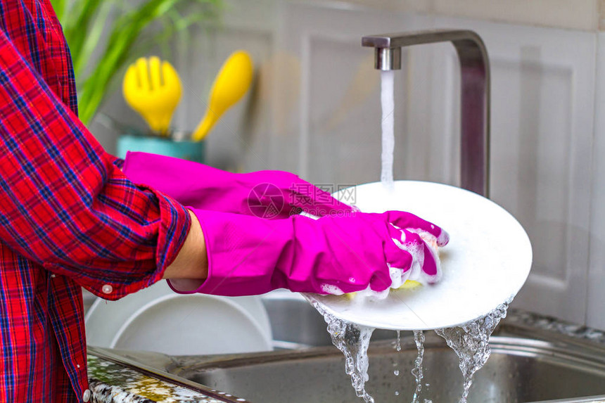 在厨房用橡皮色手套洗碗的女人亲近图片