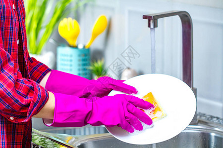 在厨房用橡皮色手套洗碗的女人亲近图片