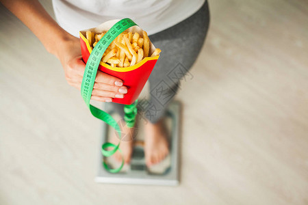 饮食在持有不健康垃圾食品的体重秤上测量体重的女人减肥图片