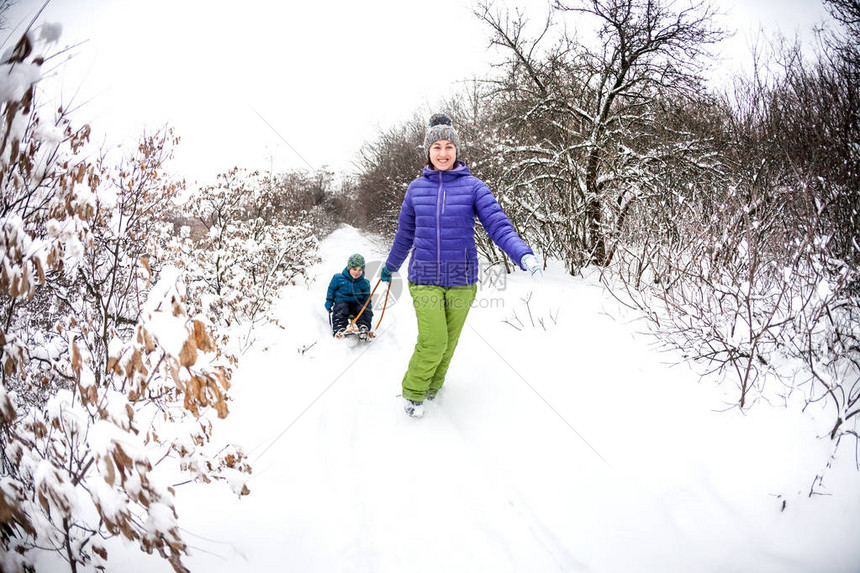 一个女人在雪橇上滚一个男孩一个孩子和他的母亲一起穿过冬天的孩子骑着雪橇穿过雪地寒假与父图片