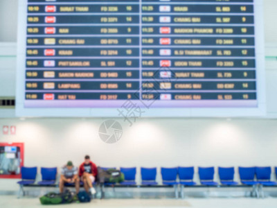 模糊的登机时间监测屏幕和乘客坐在机场大厅候机楼内端的蓝色椅子上图片