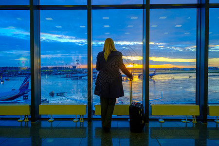 女人站在机场的窗户边日落背景背景图片