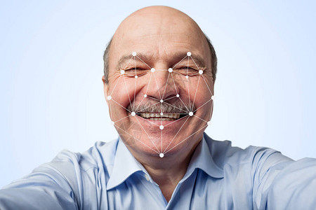 留着小胡子的老人拿着智能手机通过面部识别面部的未来主图片