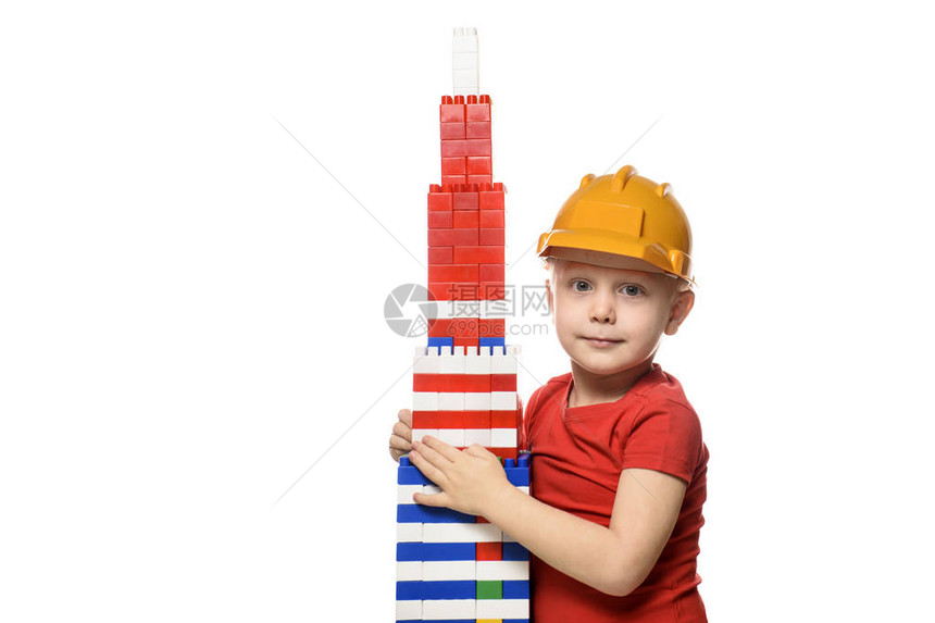 建筑头盔上的小金发小金发男孩和在塔楼附近用零件设计师建造的一件红色衬衫Pr图片