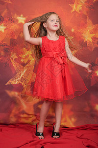 穿着红色晚礼服和母亲高跟鞋的漂亮可爱的白人小女孩站在橙色背景上图片
