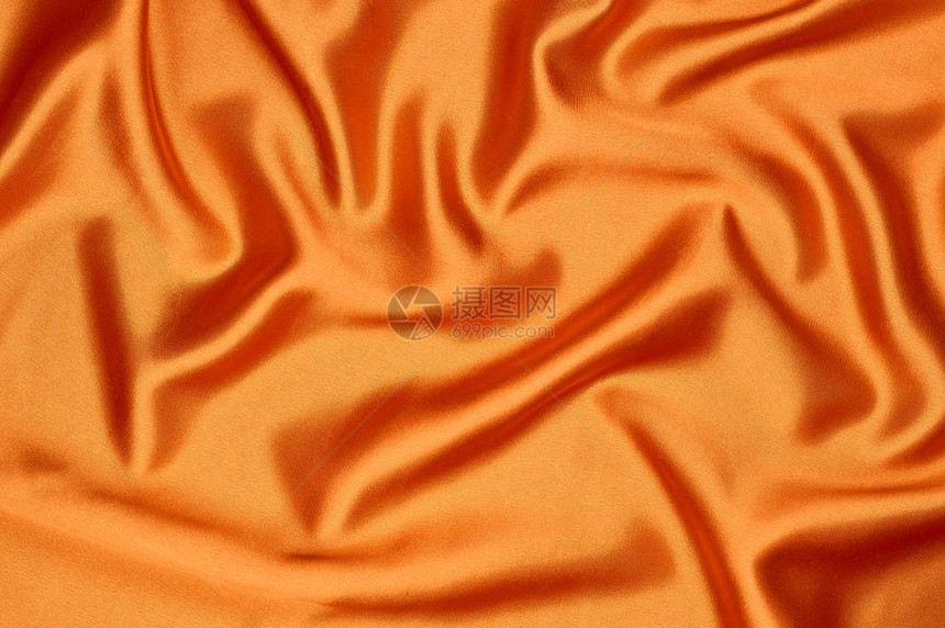 明亮的橙色丝绸面料在浅色背景纹理上溢出图片
