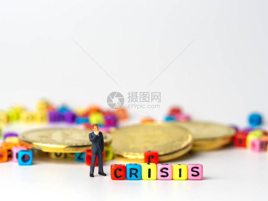 身穿深蓝色西装的微型人物商人站在CRISIS字母和金币多彩的背后图片