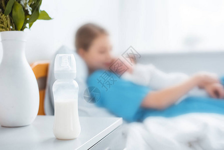 婴儿奶瓶与牛奶花瓶和母亲与新生儿躺在医院病床上后图片