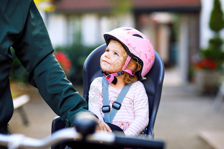 头戴安全头盔的蹒跚学步的小女孩坐在自行车座椅上背景图片