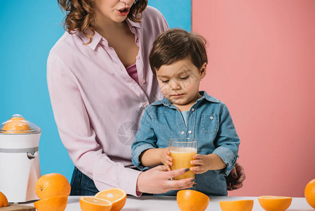 可爱的小可爱男孩喝着杯子满了鲜橙汁从母亲的图片