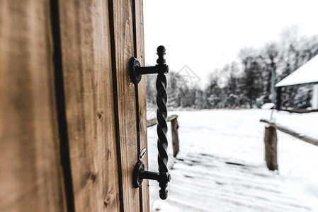 以铁脚柄和背景的雪地为背景的打开木制门有图片