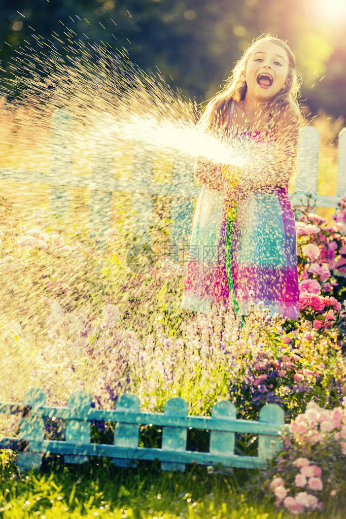 俏皮的女孩在夏天的一天在花园里用雨浇花孩子在阳光明媚的日子在日落时使用花园软管小园丁图片