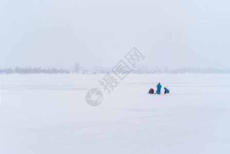 远处的三个渔民在雾蒙的雪冬景观中进行冰钓图片